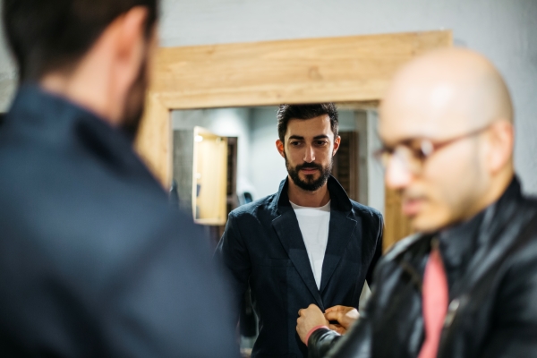 Man with client wearing new stylish suit in front of mirror