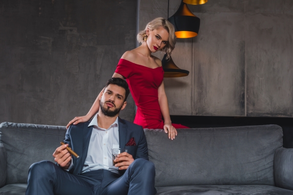 man in suit holding cigar and glass of whisky while spending time with girl