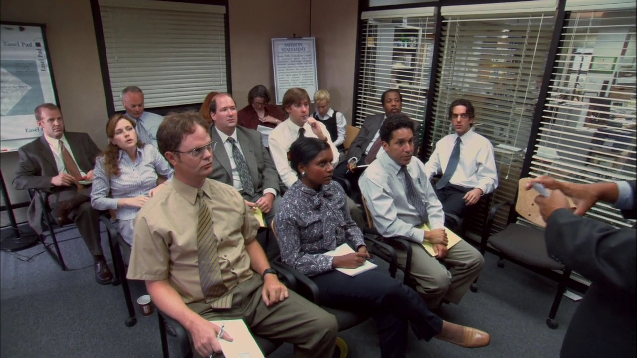 Image from The Office US with multiple characters sat in the conference room Image from The Office US with multiple characters sat in the conference room