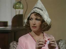 Margo staring off to the distance wearing a paper hat made from The Telegraph newspaper