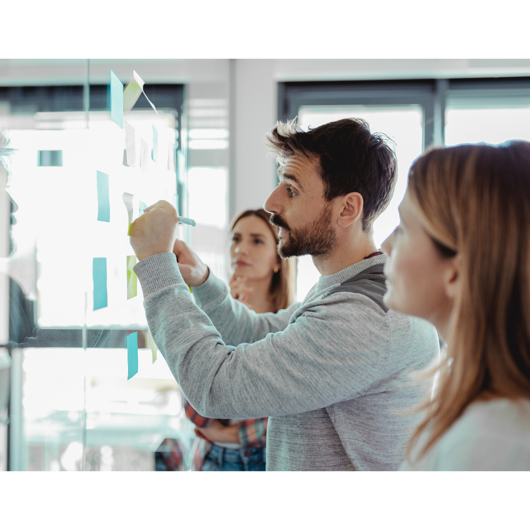 Team of business professionals identifying client's key pain points in a collaborative brainstorming session, using sticky notes on a glass wall.