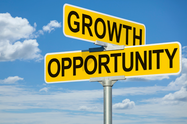 Road sign with 'Growth' and 'Opportunity' against a blue sky with clouds, illustrating business expansion directions.