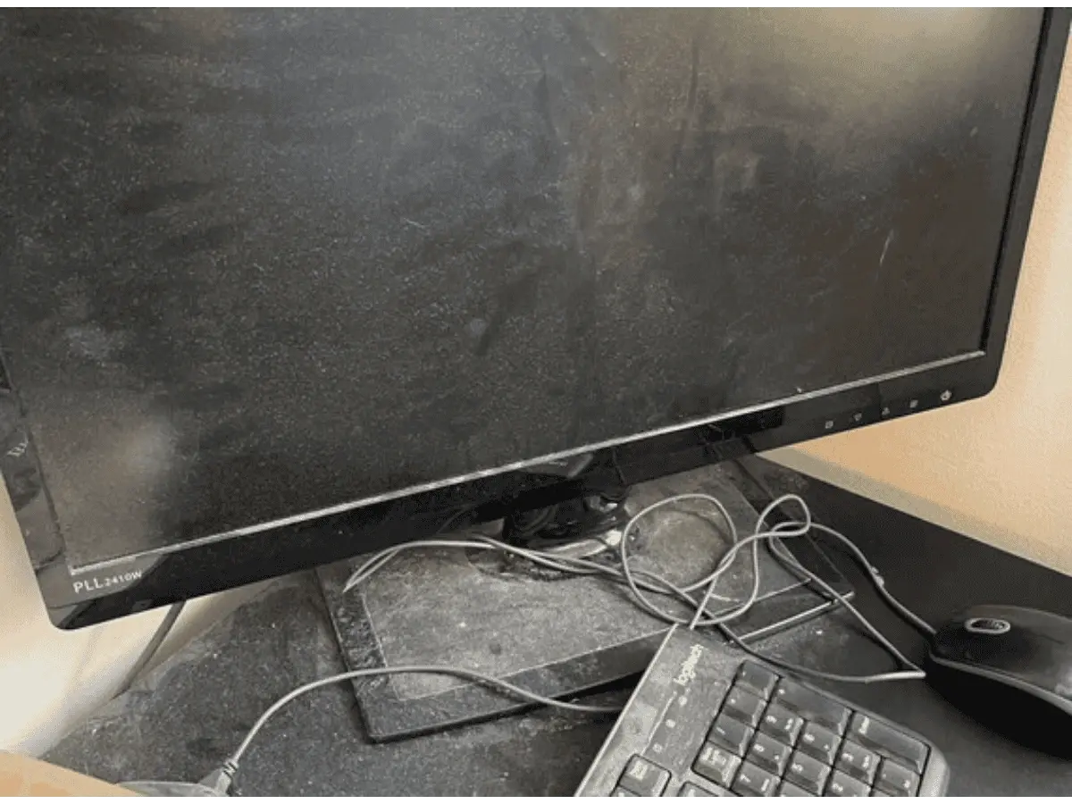 alt="Before photo of a home office desk in Maryland, covered in a thick layer of dust on the monitor, keyboard, and surfaces."