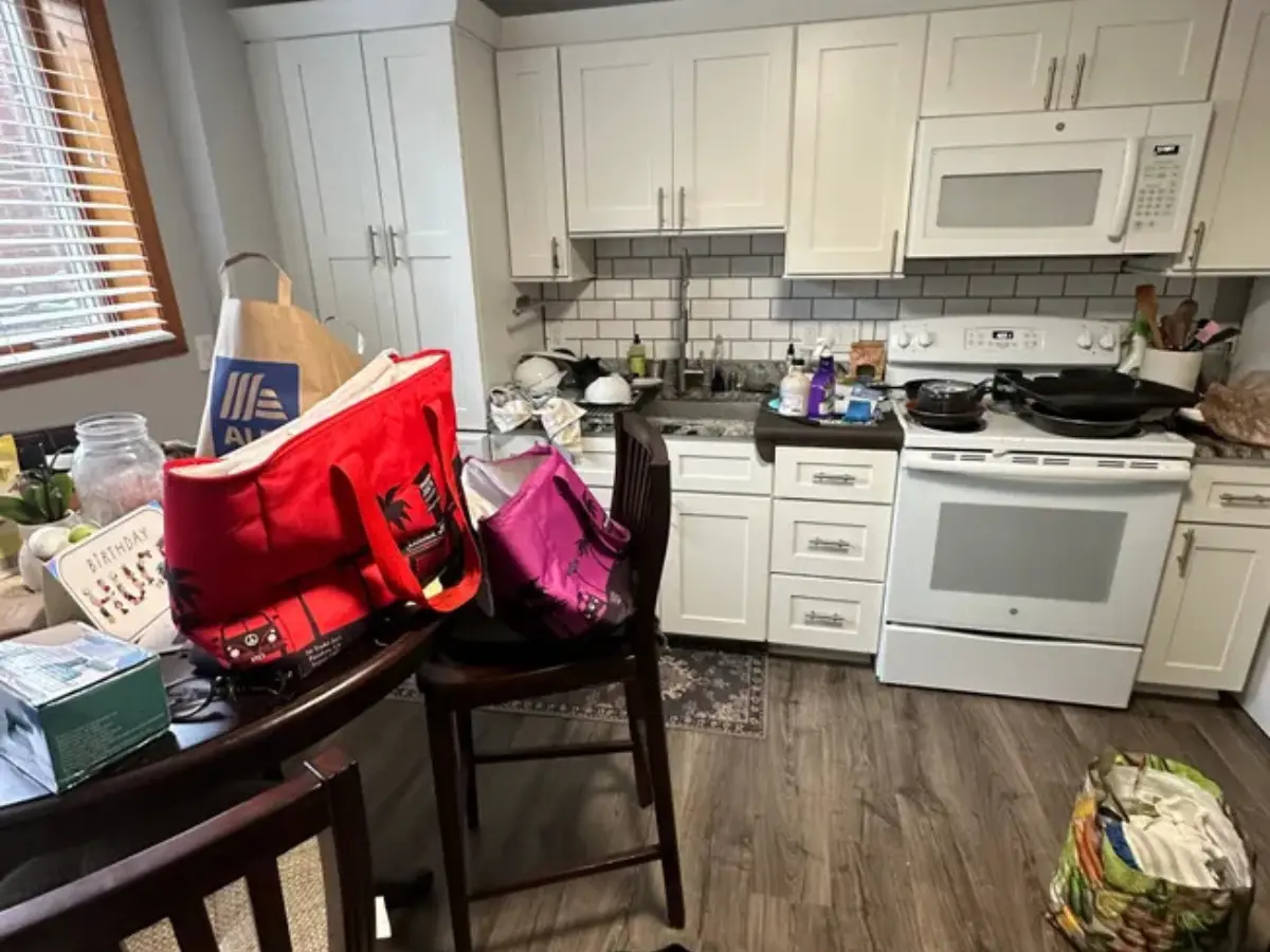 alt="A messy kitchen with groceries and bags on the counter and floor before a professional cleaning service."