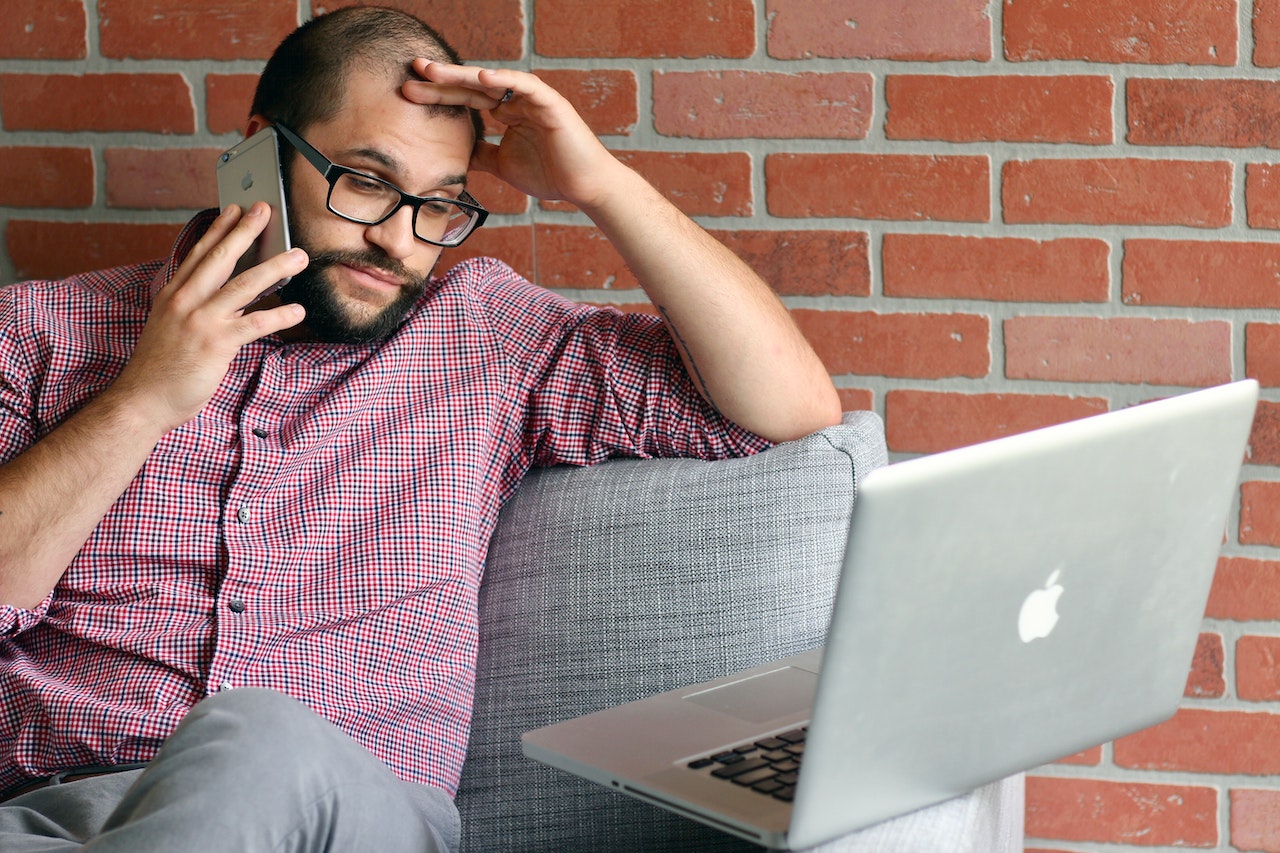 Frustrated man on phone scratching head with laptop in front of him