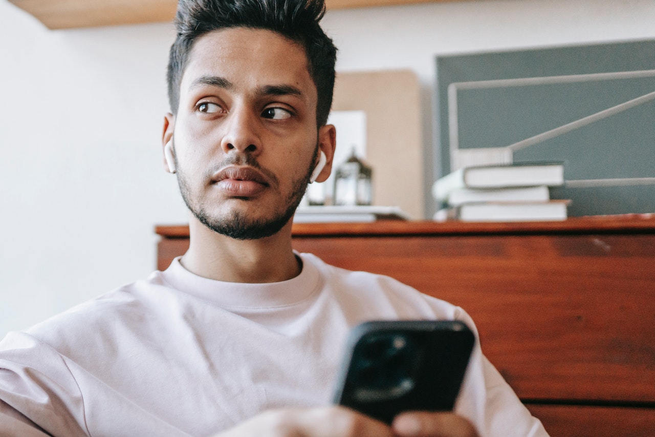 Young man sitting on couch holding phone and listening on ear pods