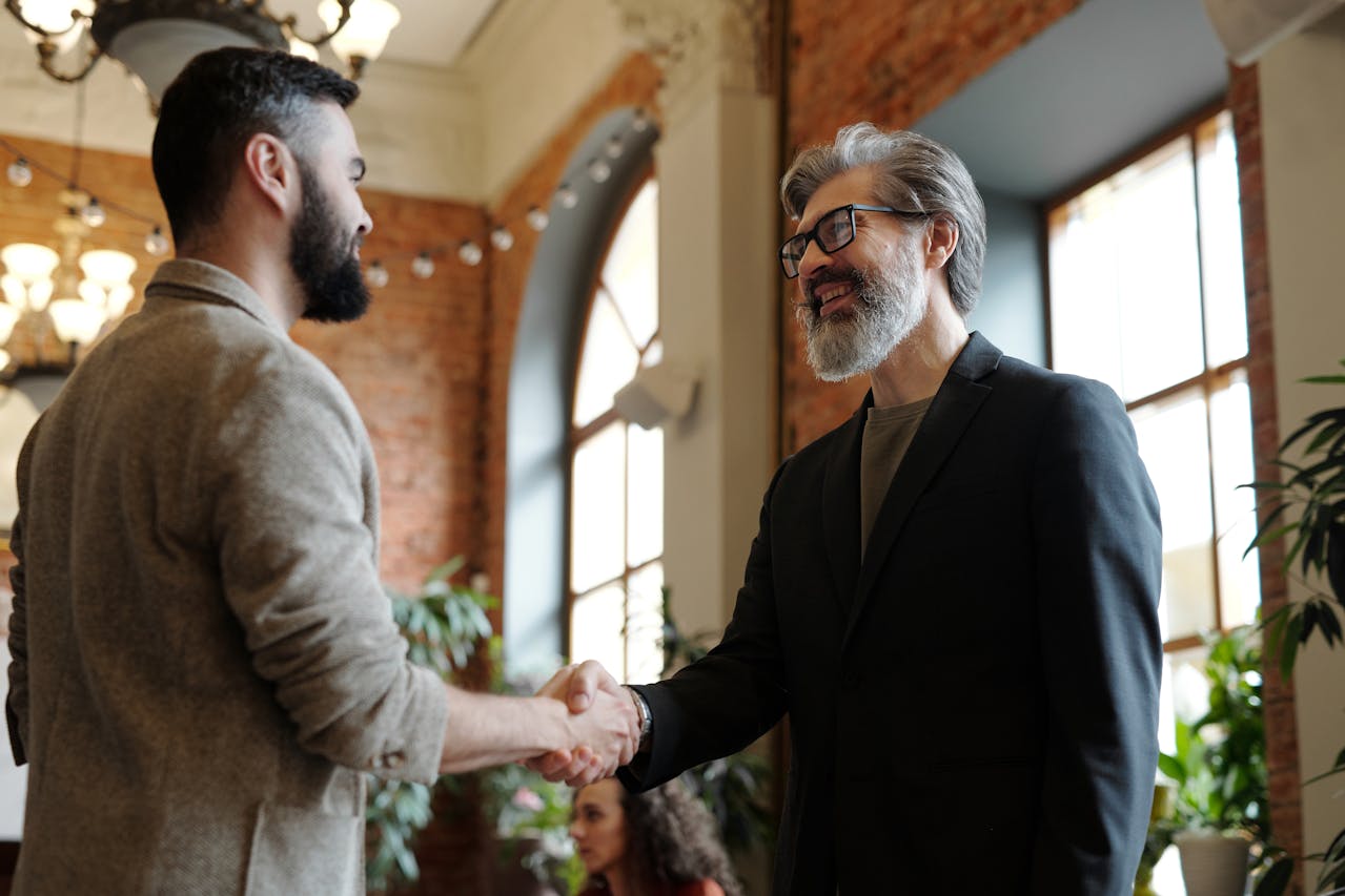 A younger and older man shaking each other's hands while smiling