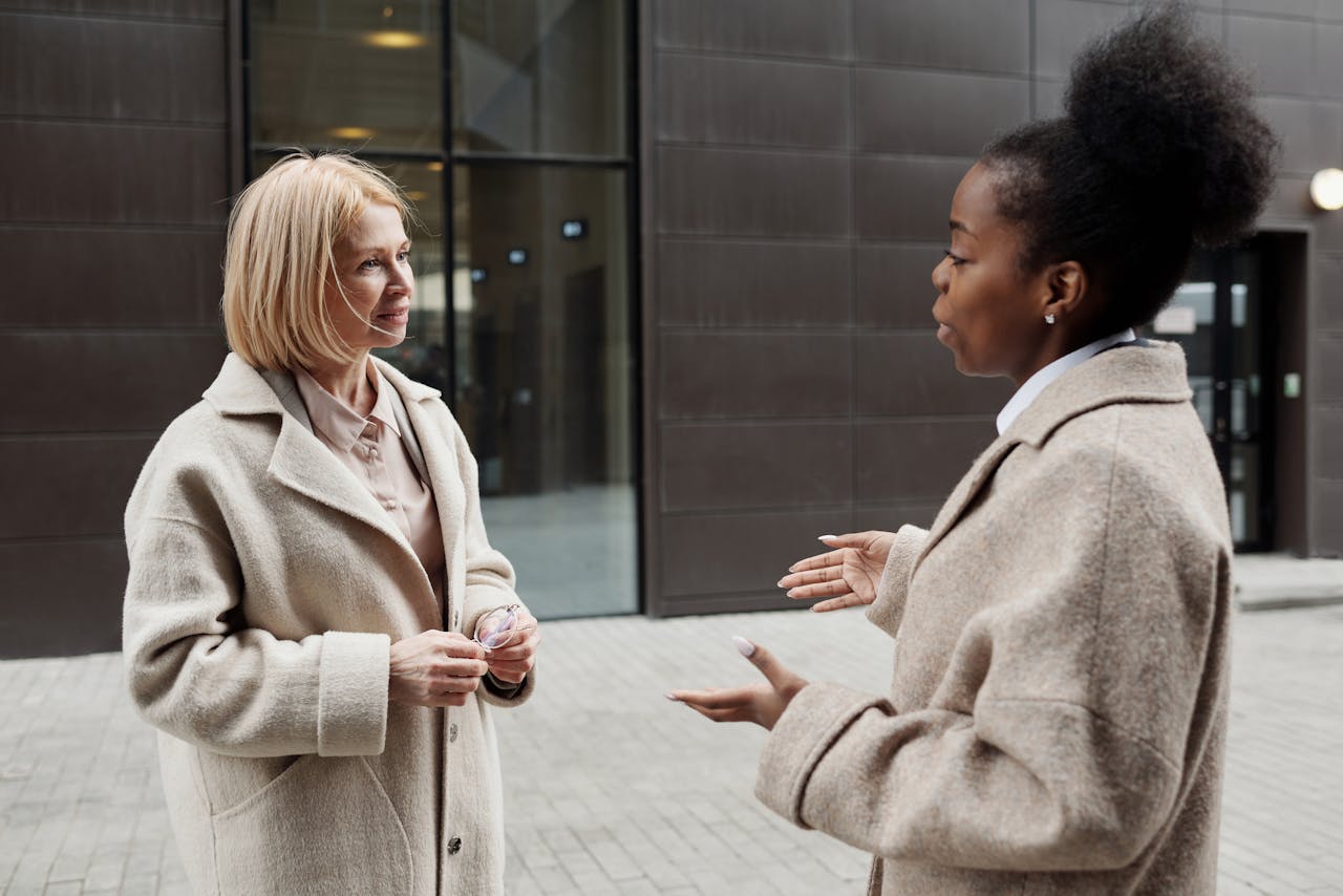 Two females discussing while standing in street and wearing jackets