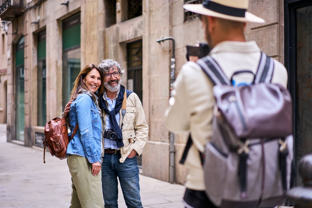 Young male photographer taking holiday photo happy elderly tourist couple posing smile city street