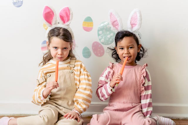 2 girls wearing bunny headbands and eating carrots