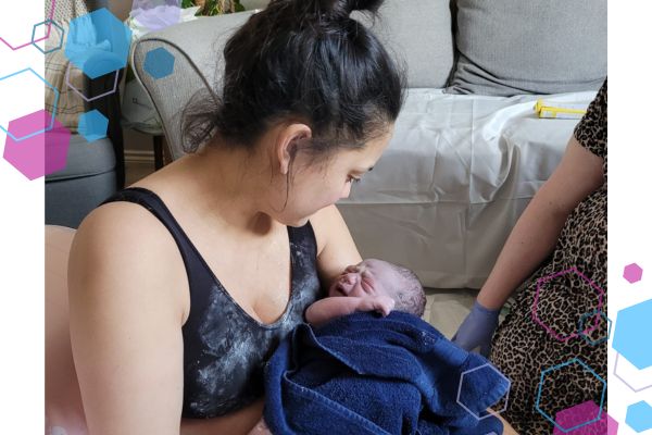 Suzy sitting on the floor cradling her newborn son just after her home birth in Welwyn Garden City