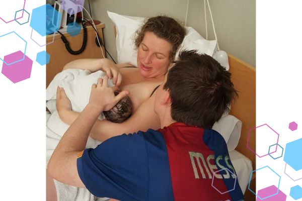 Jilly, CubCare founder in bed after her second birth cuddling and staring at her newborn. The dad is sitting next to the bed, back to the camera, looking at baby too.