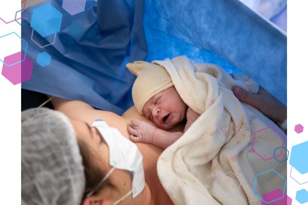 A c-section delivery where mum is lying on the operating table holding her newborn baby in skin-to-skin. Mum is wearing a mask and a hair net