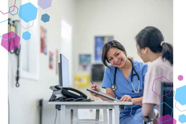 CubCare blog post important questions to ask at a midwife appointment. Image is of a woman wearing scrubs with a stethoscope around her neck. She is sitting at a desk with a pen in her hand smiling at a woman she is caring for. CubCare blog post important questions to ask at a midwife appointment. Image is of a woman wearing scrubs with a stethoscope around her neck. She is sitting at a desk with a pen in her hand smiling at a woman she is caring for.