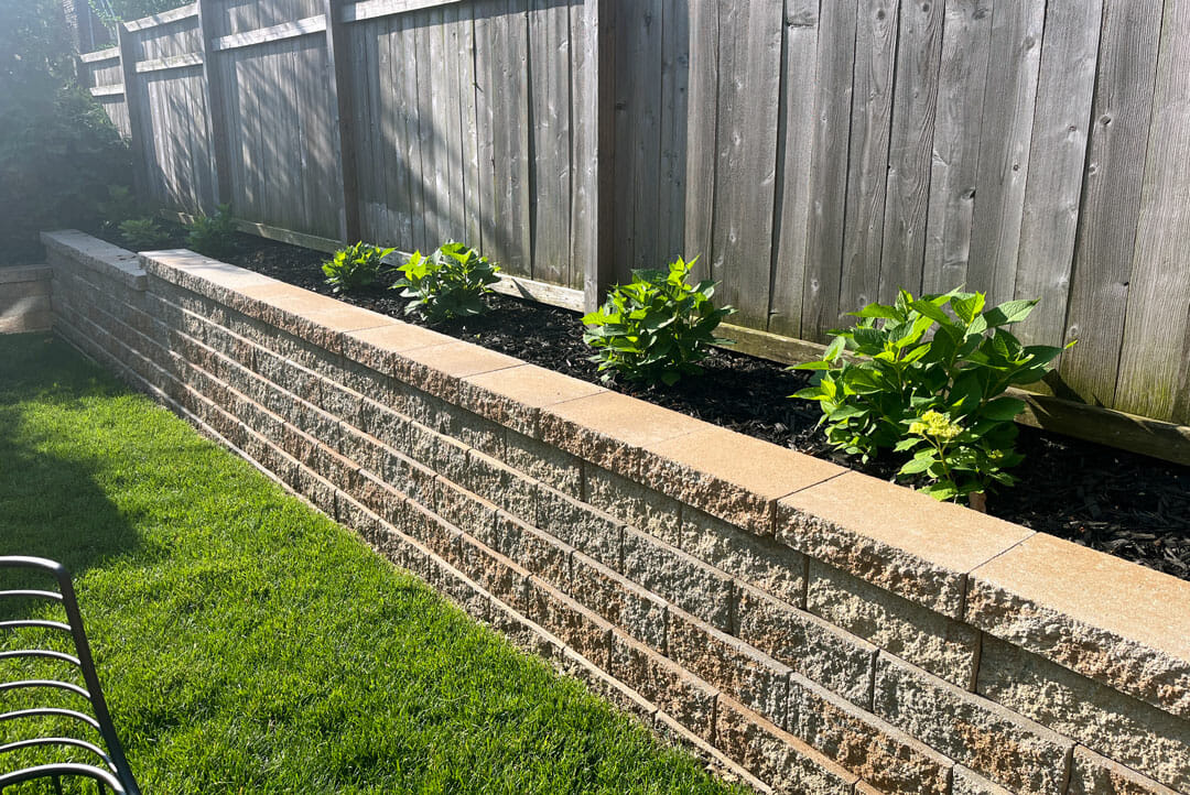Professionals working on retaining wall construction with materials visible in a residential landscape setting Professionals working on retaining wall construction with materials visible in a residential landscape setting