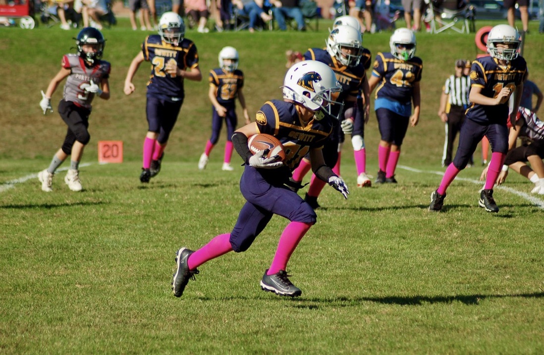 Youth football player sprinting across the field with the ball, symbolizing drive, momentum, and the importance of strategy and consistency in business growth.