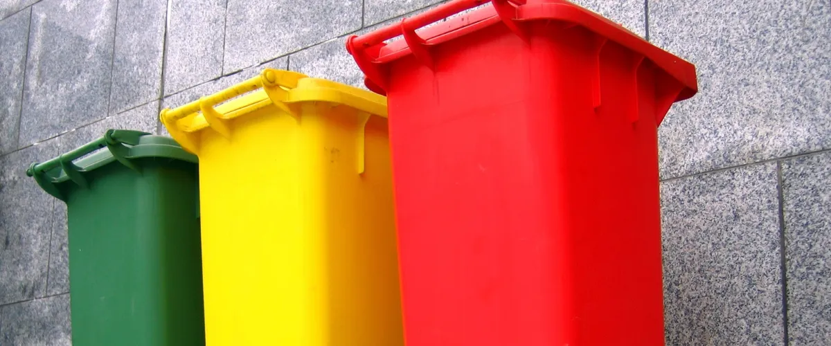 Color-coded recycling bins in green, yellow, and red against a gray wall Color-coded recycling bins in green, yellow, and red against a gray wall