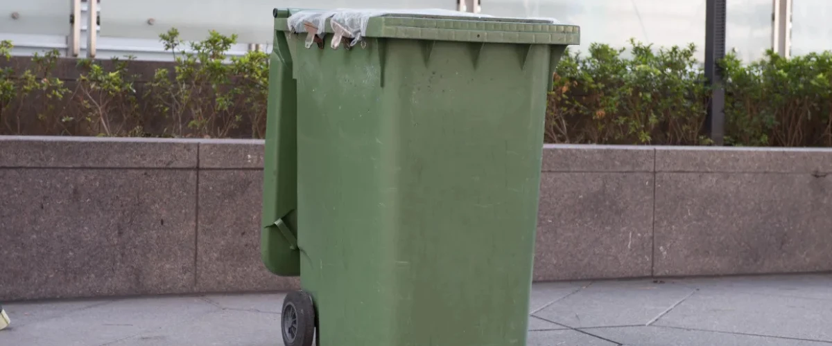 Large green outdoor garbage bin on city sidewalk.