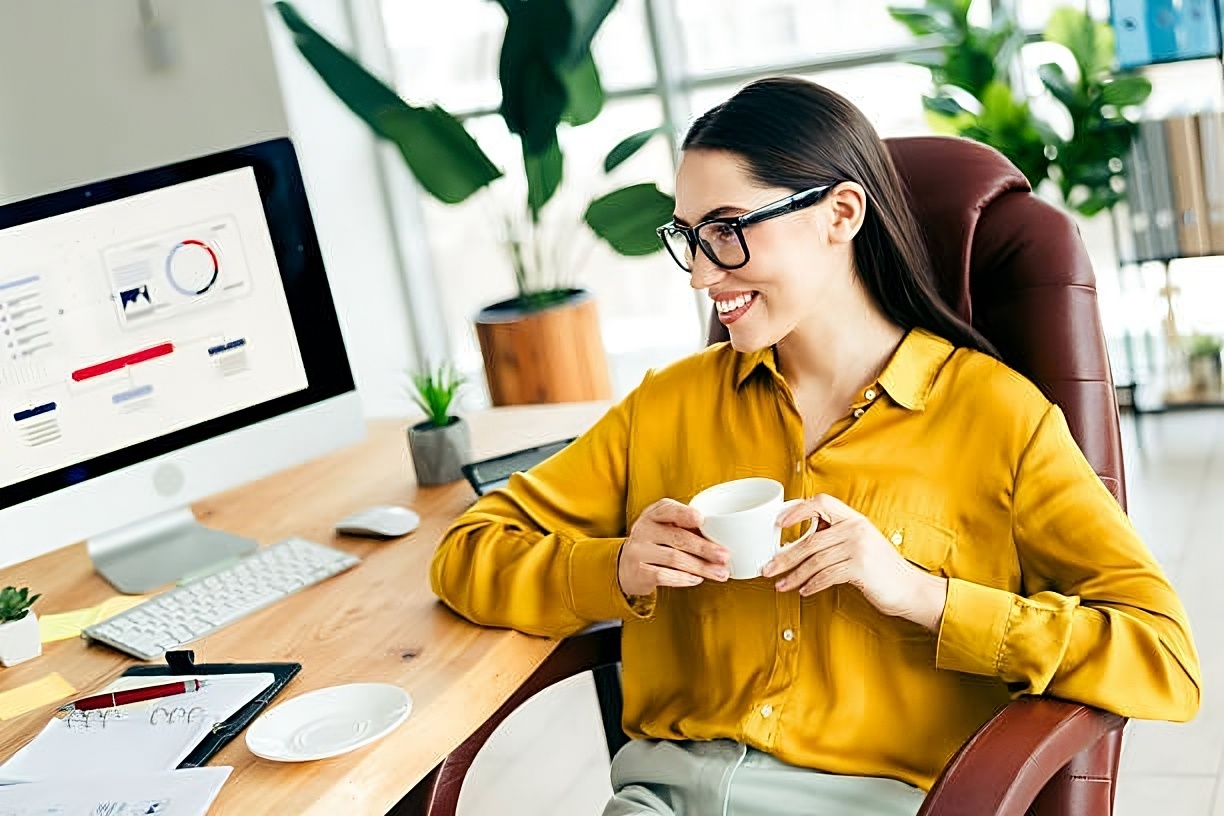 A happy accountant sipping coffee at a tidy desk while her computer shows automated tools working