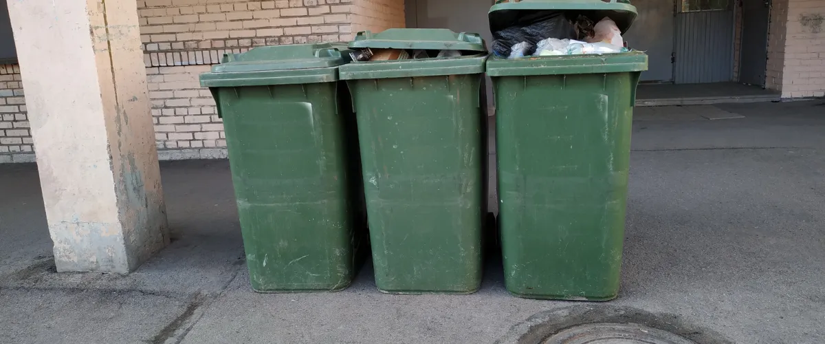 Row of green outdoor trash bins overflowing with garbage in an alleyway