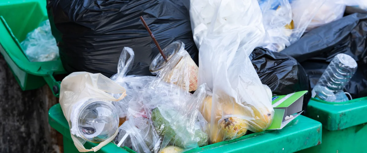 Overflowing green trash bin filled with food waste and plastic bags