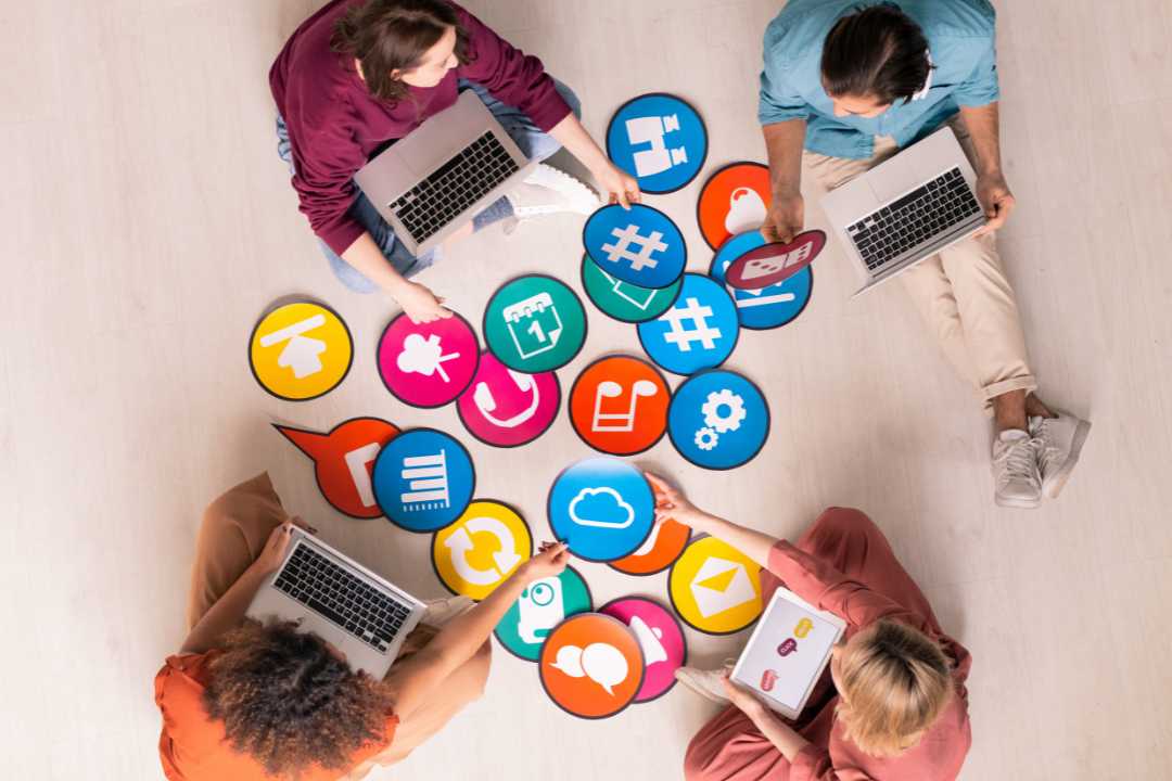 Top-down view of a diverse group of professionals collaborating on digital marketing strategy, using colorful social media and communication icons while working on laptops and tablets. Top-down view of a diverse group of professionals collaborating on digital marketing strategy, using colorful social media and communication icons while working on laptops and tablets.