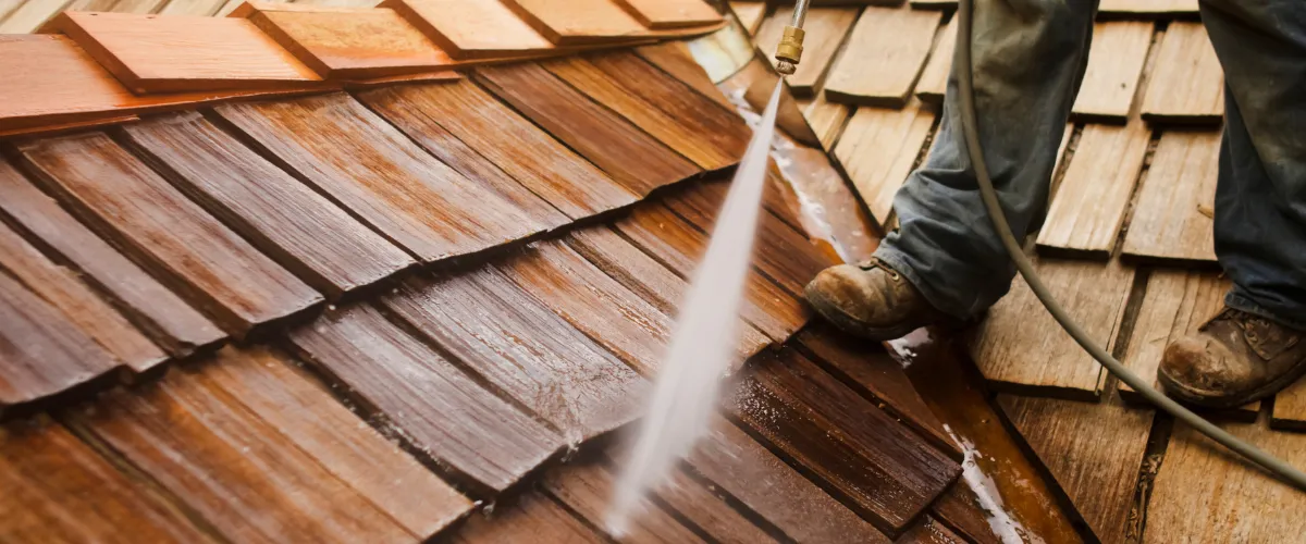 Pressure washing wooden shake roof with worker wearing boots
