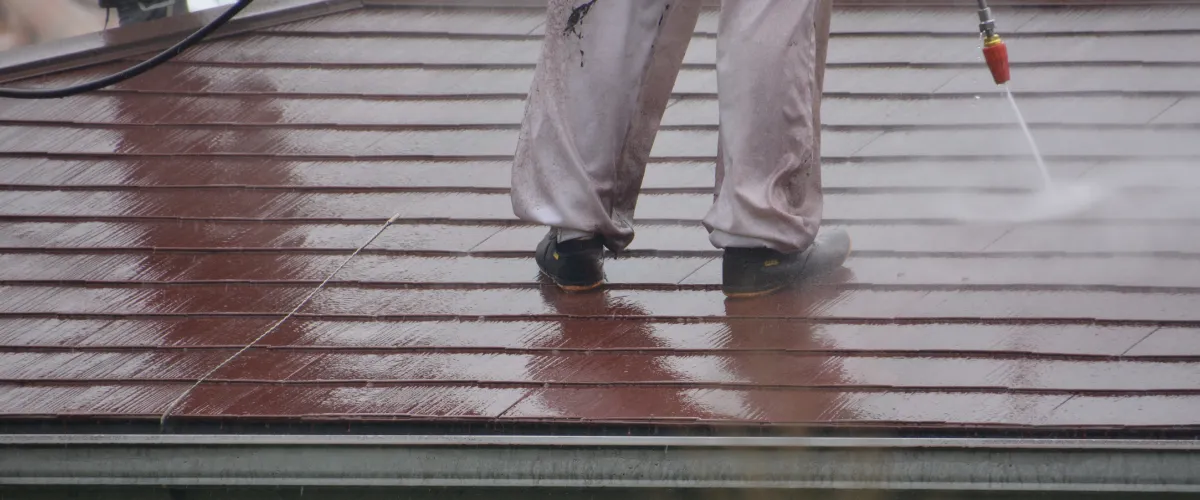 Worker pressure washing a house roof to remove buildup and grime