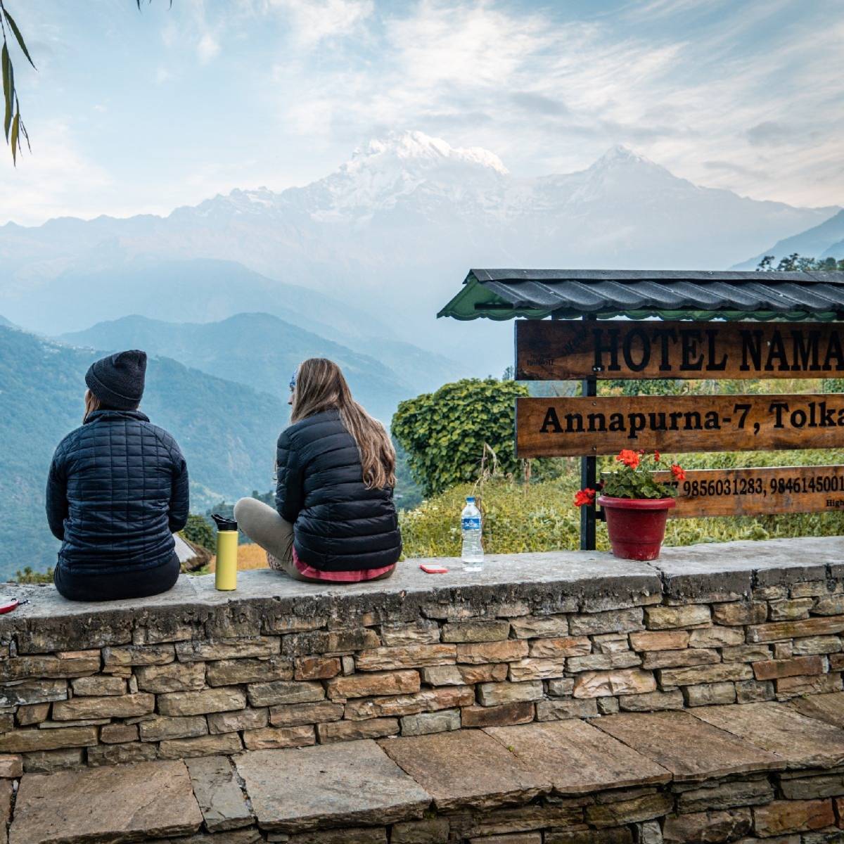2 people sitting on a ledge, overlooking the Himalayas.