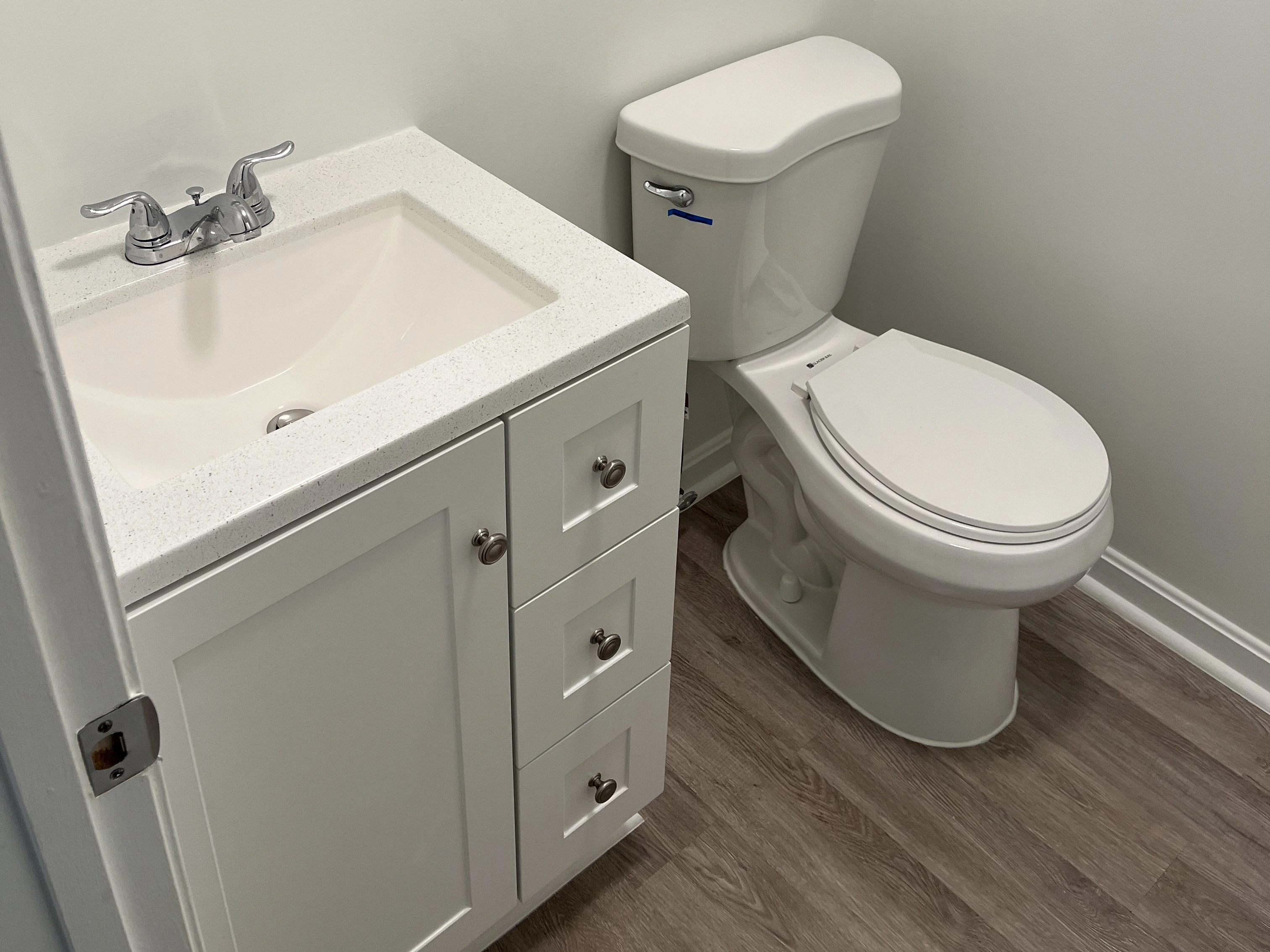 A modern bathroom features a white sink with a chrome faucet and a matching toilet, set against light-colored walls and wooden flooring.