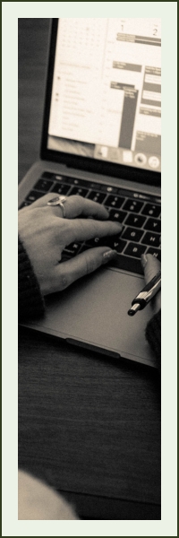 An over-the-shoulder view of a woman's hands on a laptop keyboard as she manages a Google calendar.