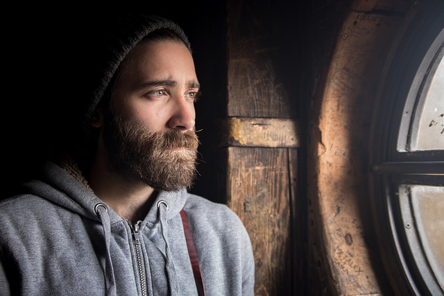white bearded man in beanie looking out window