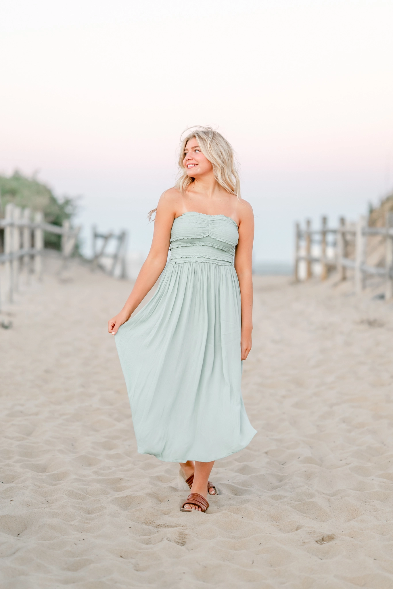 A high school senior, in a mint green sun dress, walks along Sandbridge beach during her senior portrait session.