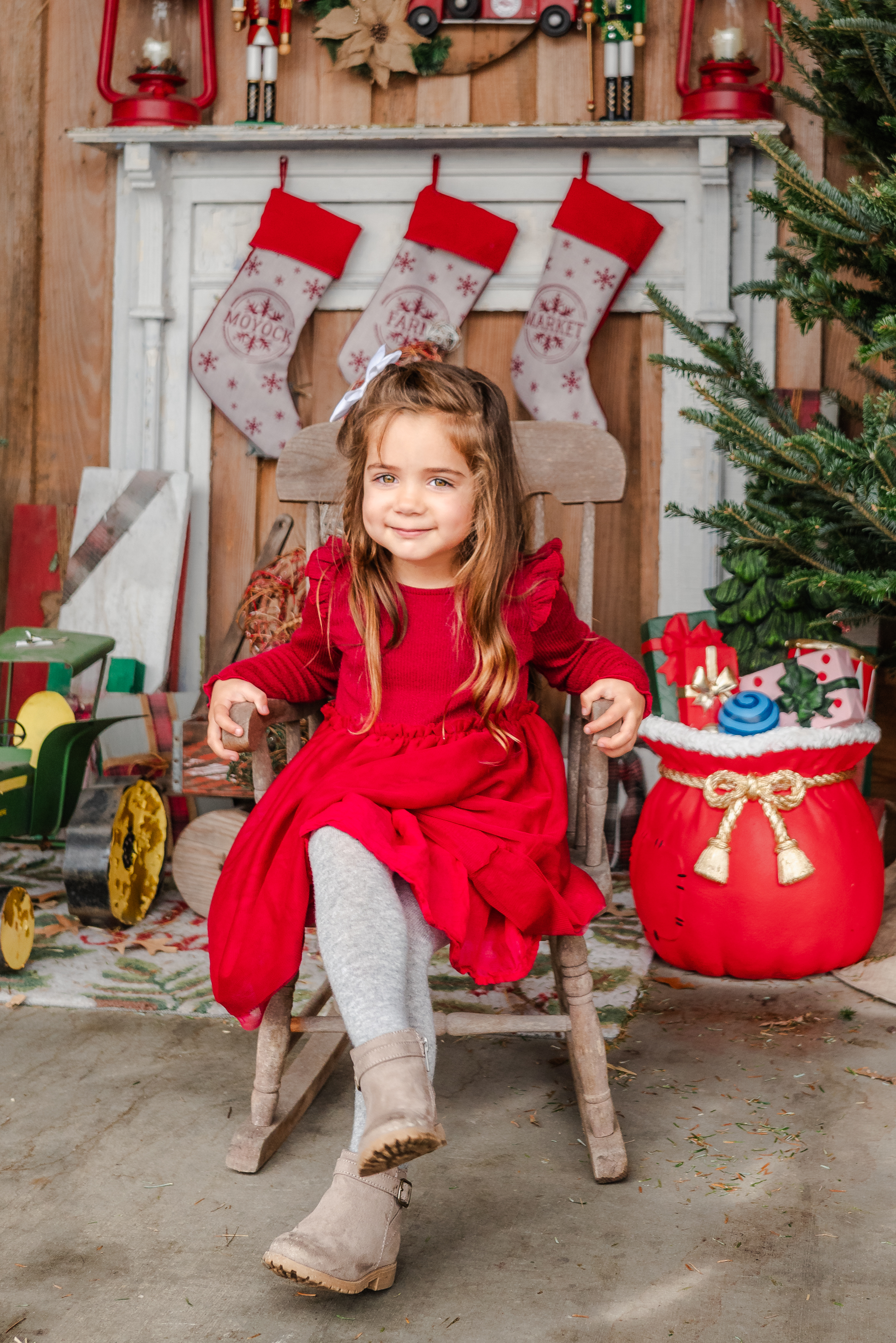 A toddler in a Christmas dress sits in a small rocking chair during her Christmas mini session in Chesapeake.
