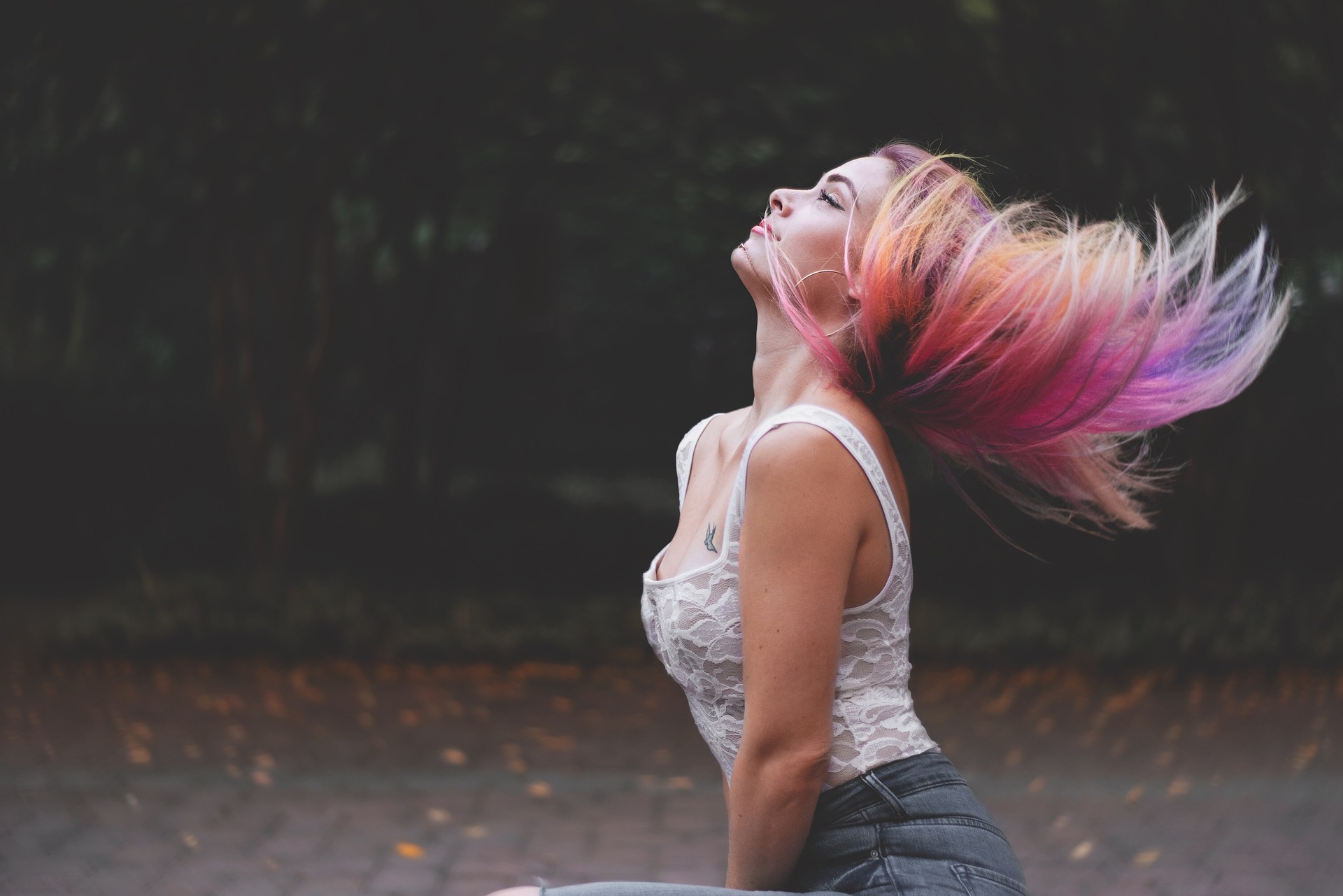 A woman with vibrant, multi-colored hair in shades of pink, purple, and yellow, capturing the essence of 2024's bold and expressive hair color trends. She is outdoors, in a moment of freedom and movement, embodying the personal style and creativity celebrated in the latest hair fashion.
