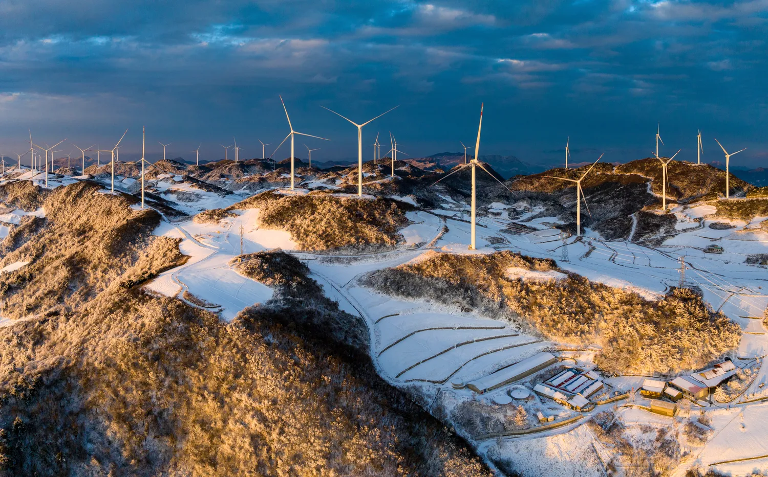 A large wind farm in Yichang, China, with dozens of white wind turbines arranged across a hillside with mountains in the background. A large wind farm in Yichang, China, with dozens of white wind turbines arranged across a hillside with mountains in the background.