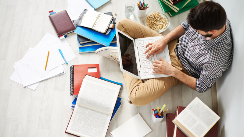 person sitting on the floor surrounded by books with laptop on lap
