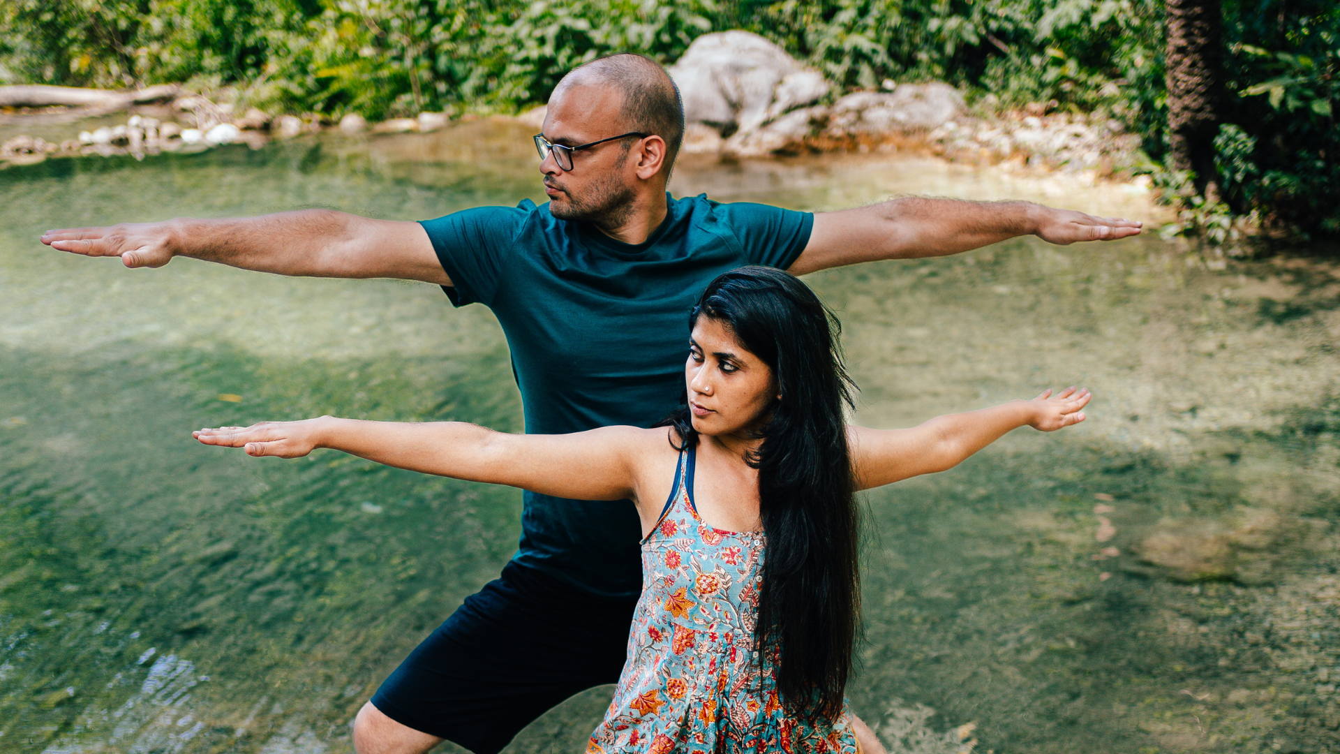 An Indian woman and man practicing Yoga in nature, in front of a river stream