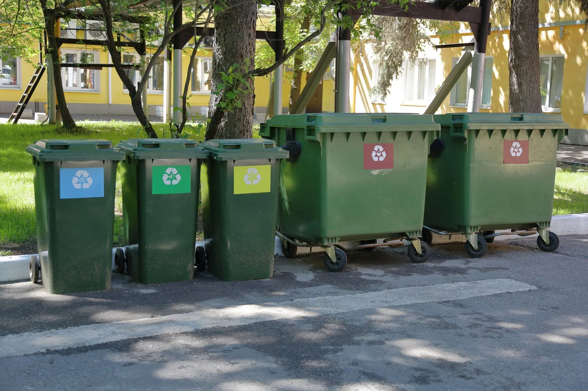 Multiple green recycling bins with color-coded labels for waste separation. Multiple green recycling bins with color-coded labels for waste separation.