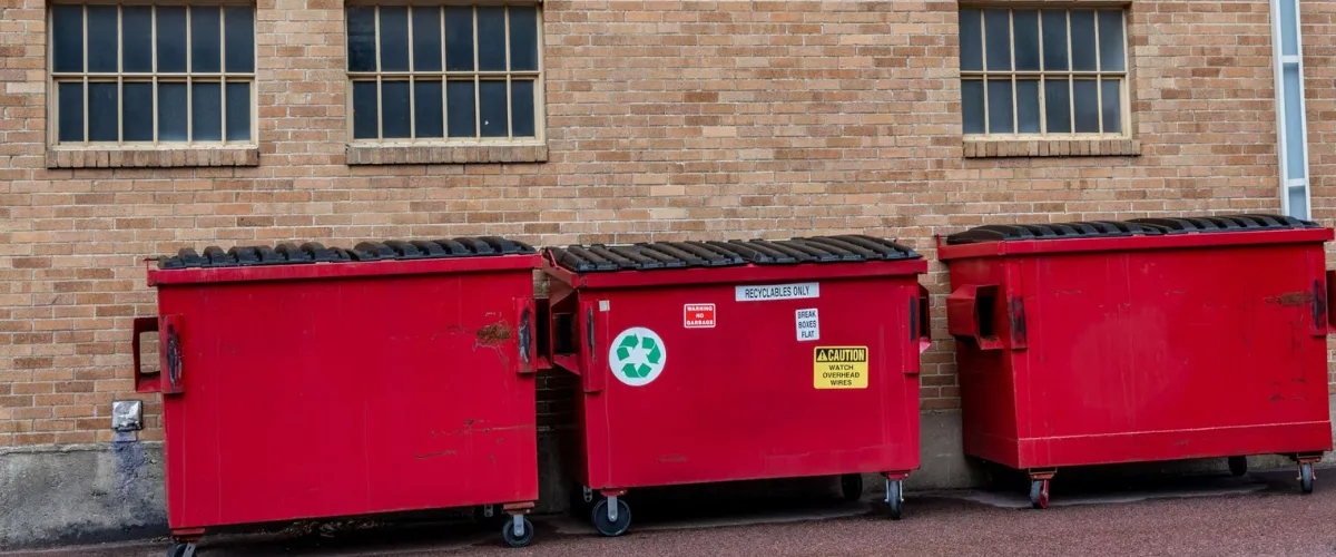Row of red commercial dumpsters against a brick wall for recycling and waste disposal