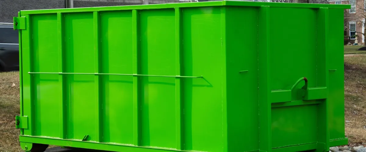 Large green commercial dumpster container on grass for waste management.