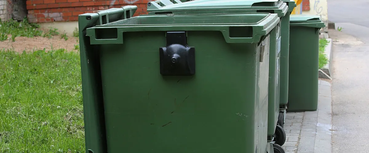 Multiple green dumpsters on pavement requiring professional cleaning