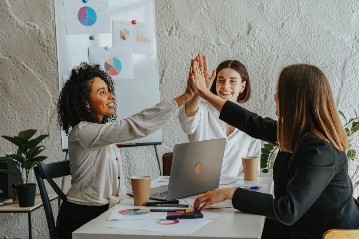 three women giving high five to each other in an office