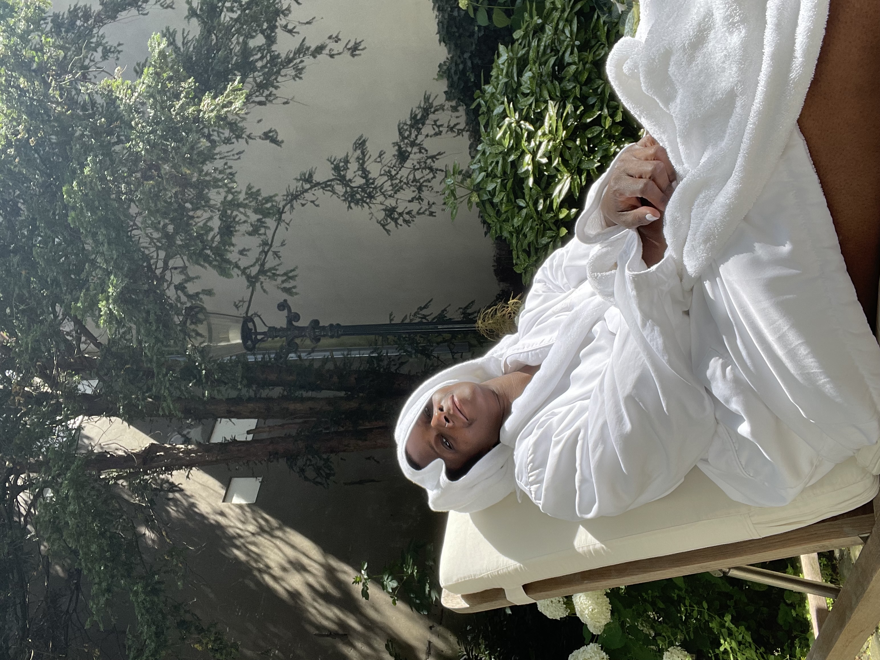 Rosalind Bigg, wearing a white robe and head wrap, is lounging at The Waldorf Astoria Hotel.
