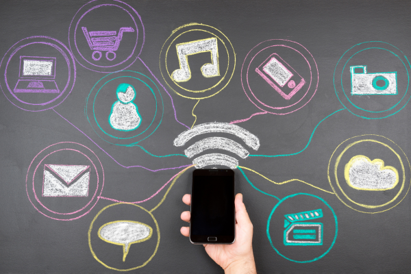 A hand holding a smartphone with chalk-drawn icons representing various online services like shopping, music, communication, and social media, connected by a central Wi-Fi symbol, symbolizing digital connectivity. A hand holding a smartphone with chalk-drawn icons representing various online services like shopping, music, communication, and social media, connected by a central Wi-Fi symbol, symbolizing digital connectivity.