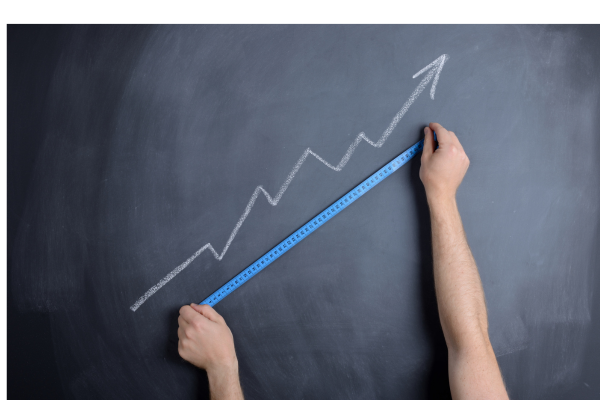 Hands holding a blue ruler against a chalkboard with an upward-trending line graph drawn in white chalk, symbolizing growth, progress, and measurement. Hands holding a blue ruler against a chalkboard with an upward-trending line graph drawn in white chalk, symbolizing growth, progress, and measurement.