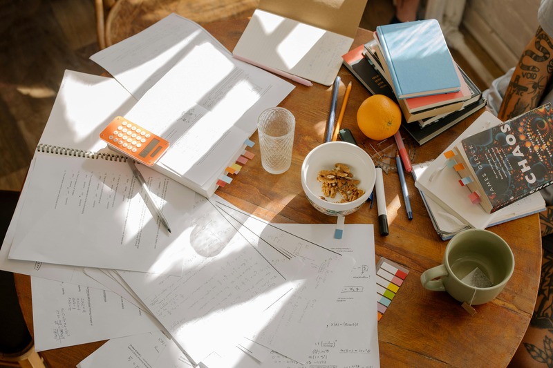 A dining table is littered with breakfast, a paper mess, a laptop and a calculator. A dining table is littered with breakfast, a paper mess, a laptop and a calculator.