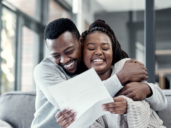 a couple hugging in relief looking at paperwork a couple hugging in relief looking at paperwork