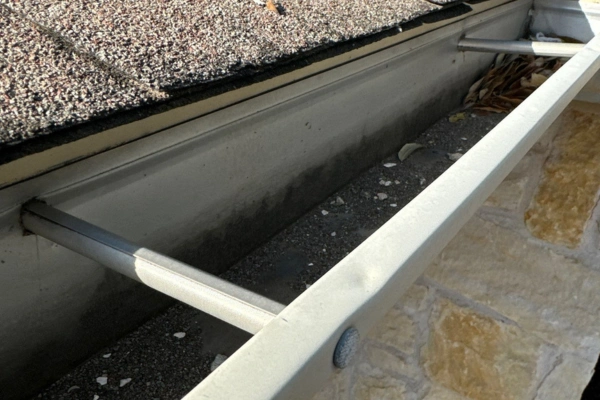 Clogged residential rain gutter with debris buildup under asphalt shingle roof, highlighting the need for professional gutter cleaning and maintenance to prevent water damage.