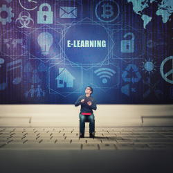 Man sitting in a chair on a laptop keyboard with the laptop screen displaying the word E-LEARNING and several apps.